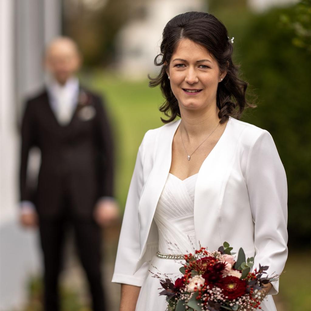 Eine Frau in einem weißen Outfit hält einen farbenprächtigen Blumenstrauß draußen vor einem unscharfen Hintergrund.